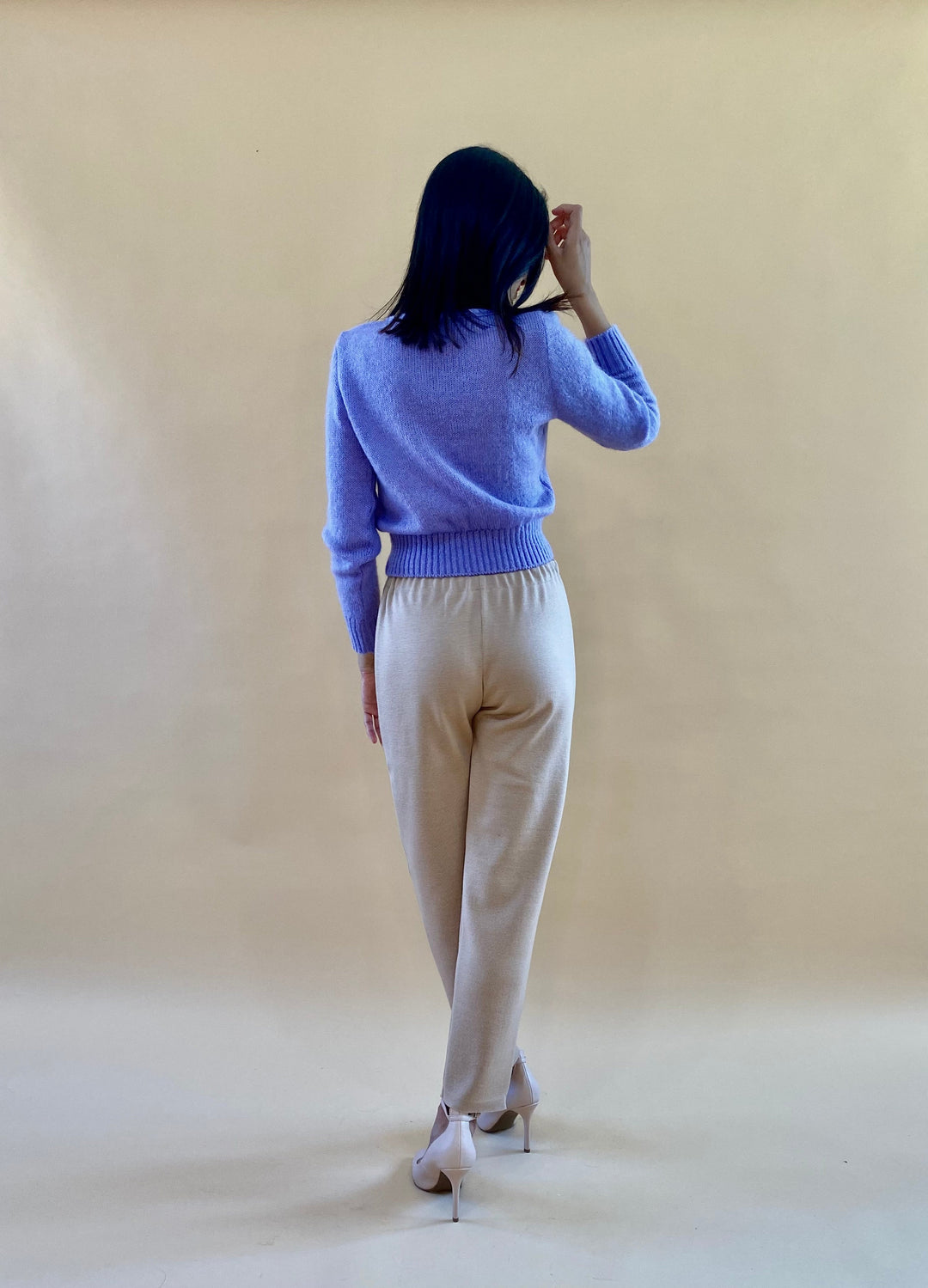 Woman modeling beige pants and a lavender sweater against a beige background