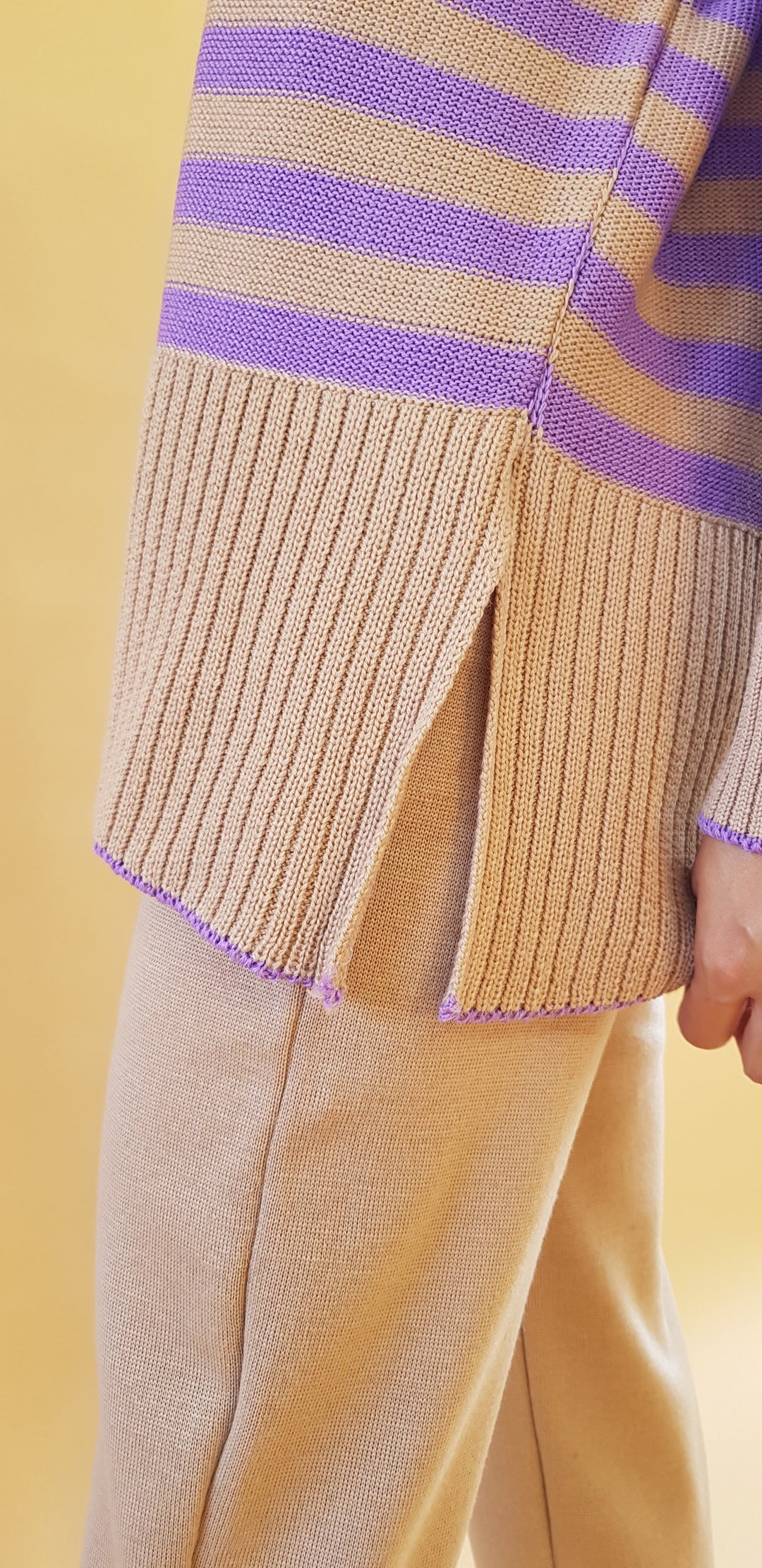 Close-up of a beige and purple striped sweater with side slit over beige pants