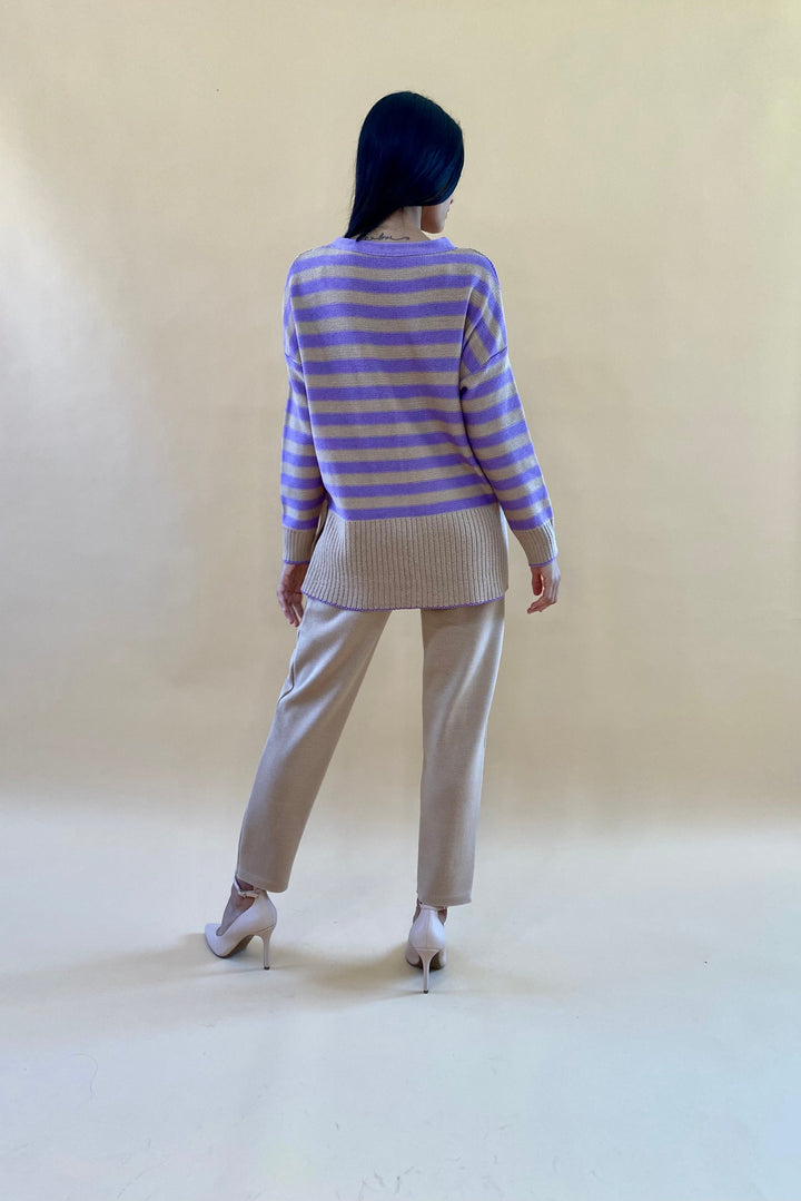 Back view of woman wearing a purple and beige striped sweater with beige pants