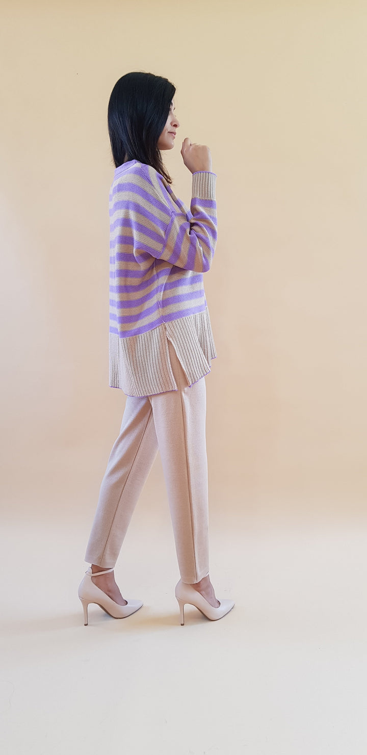 Woman wearing a purple striped sweater with beige pants and high heels, posing against a beige background