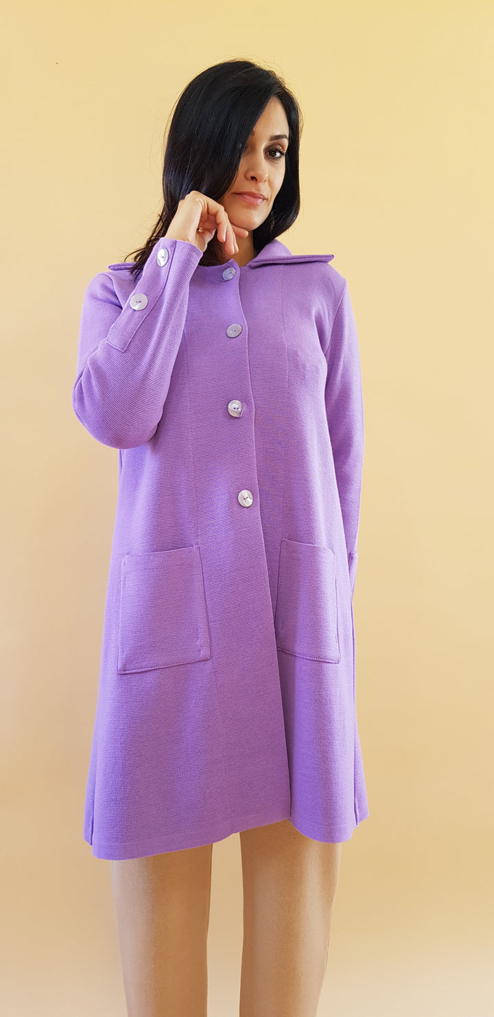 Woman wearing a purple long coat with buttons and two front pockets against a beige background
