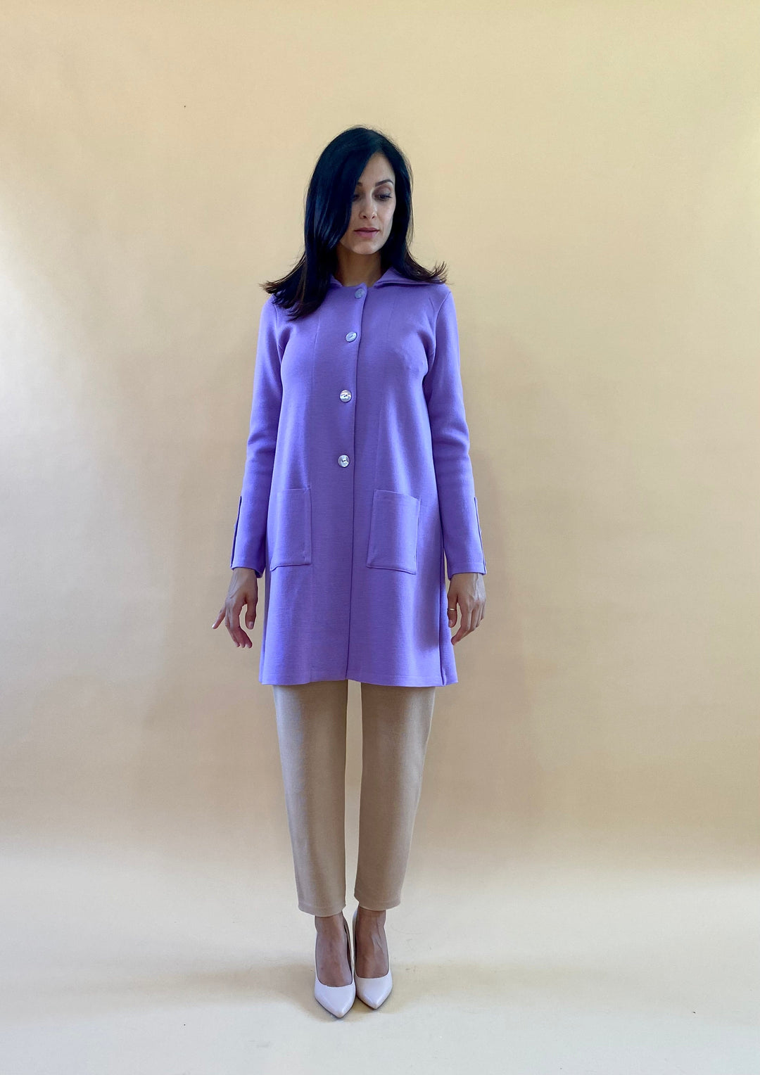 Woman wearing a purple coat and beige pants against a neutral background