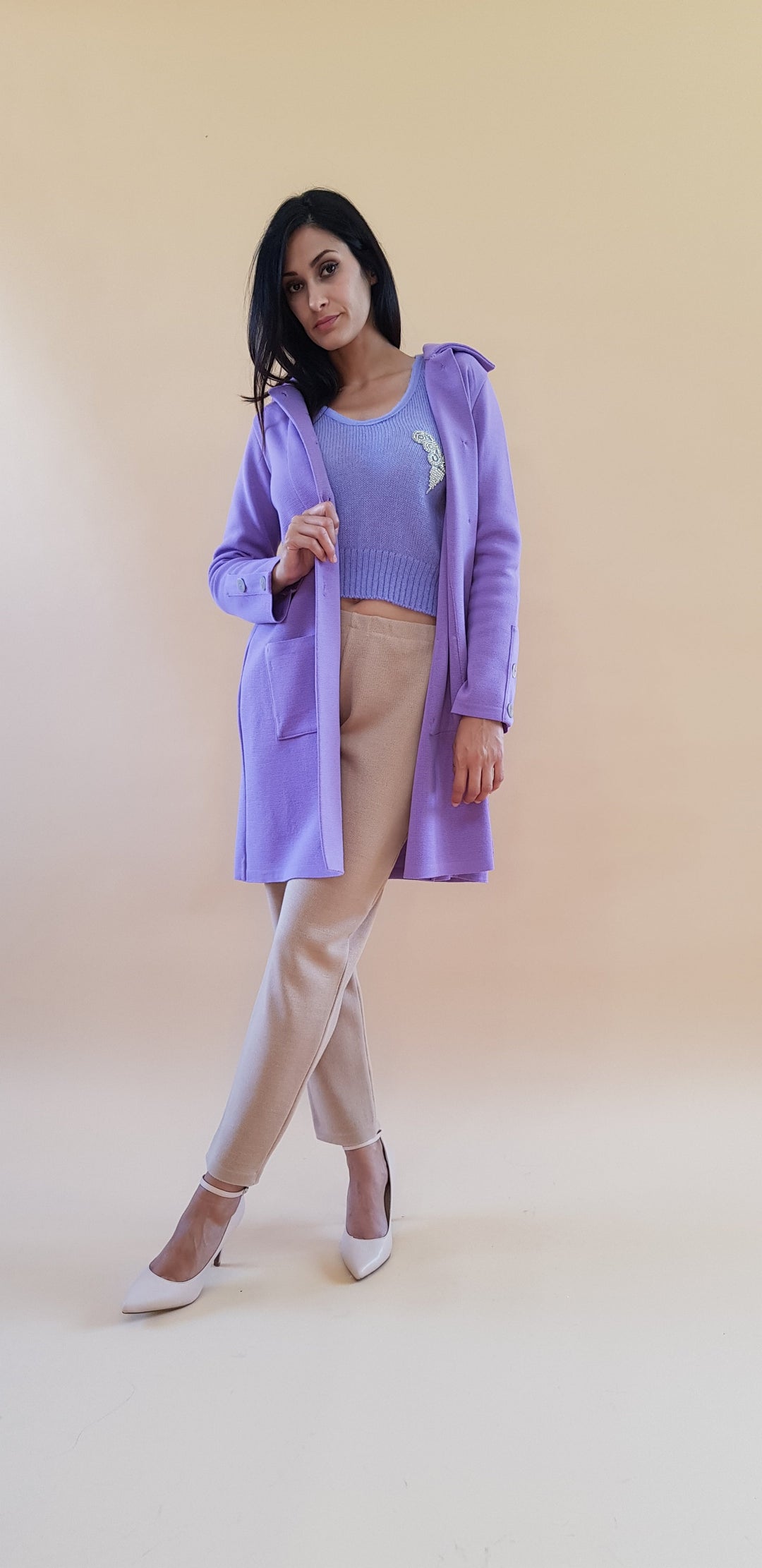 Woman wearing a purple coat with beige pants against a neutral background