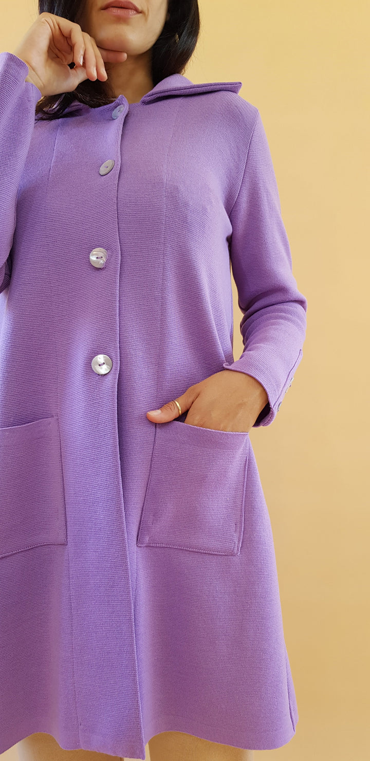 Woman wearing a long purple coat with large pockets and silver buttons