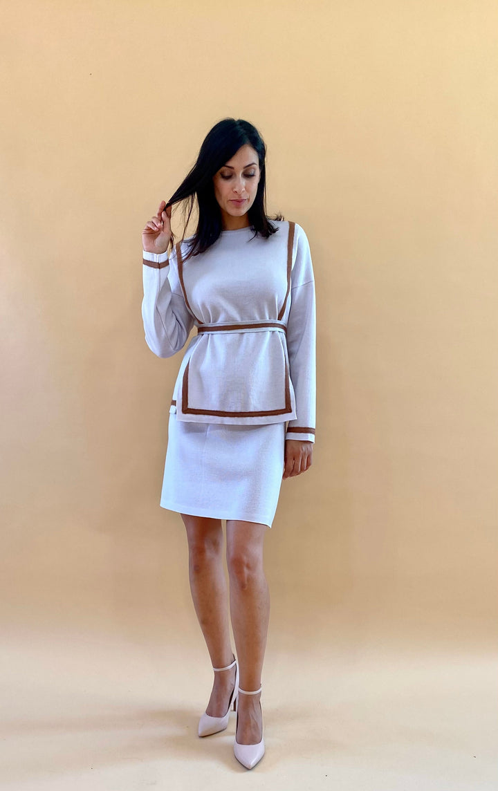 Woman in a beige sweater dress with belt and heels against a beige background