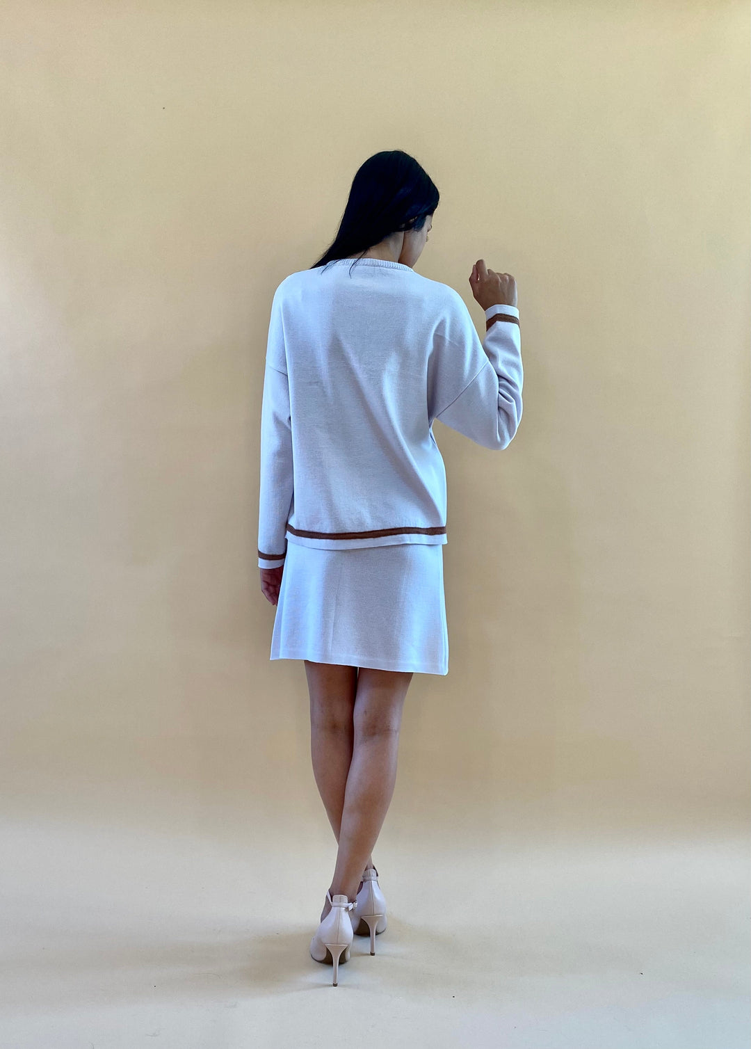 Woman wearing white dress with brown accents, standing and posing against a beige background