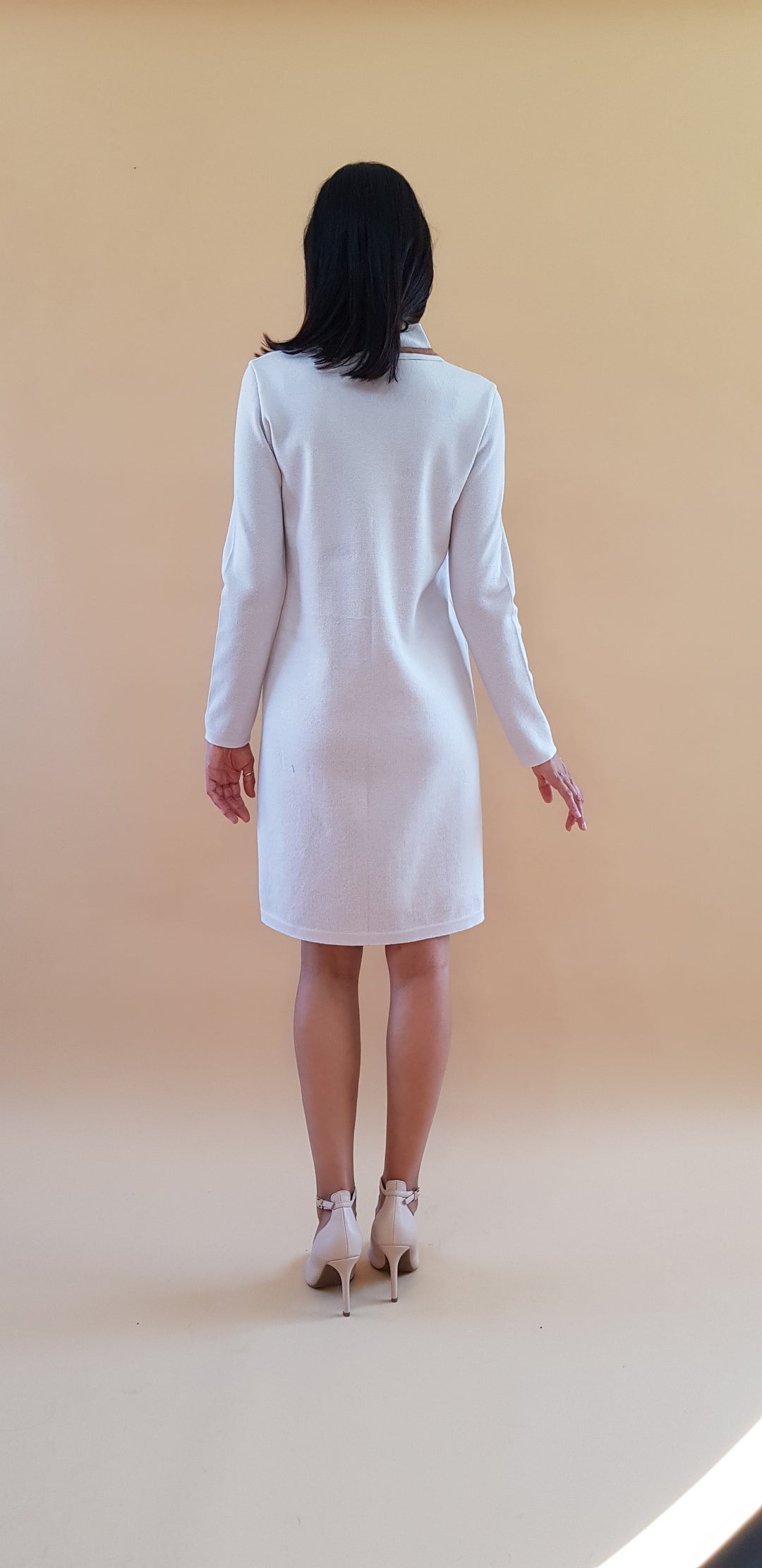 Woman in white long-sleeve dress and high heels facing away