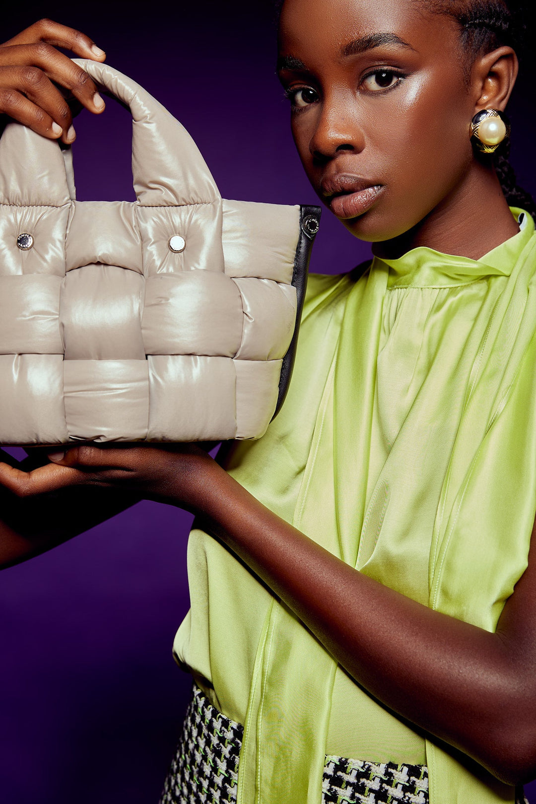 Fashion model showcasing a stylish beige quilted handbag against a purple background