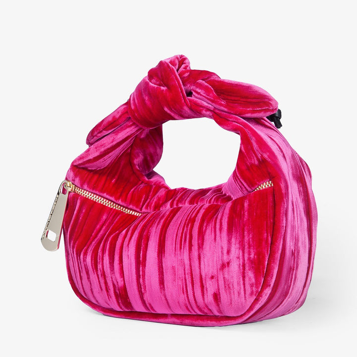 Pink velvet handbag with twisted top handle and gold zipper against white background