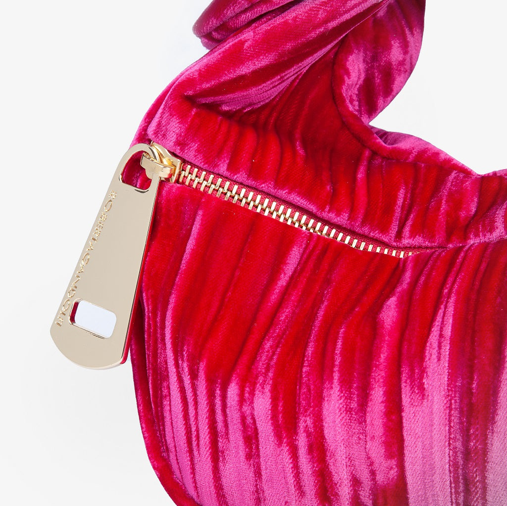 Close-up of a red velvet handbag with gold zipper and branded gold tag