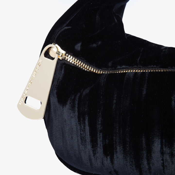 Close-up of a black velvet handbag with a gold zipper and metal tag