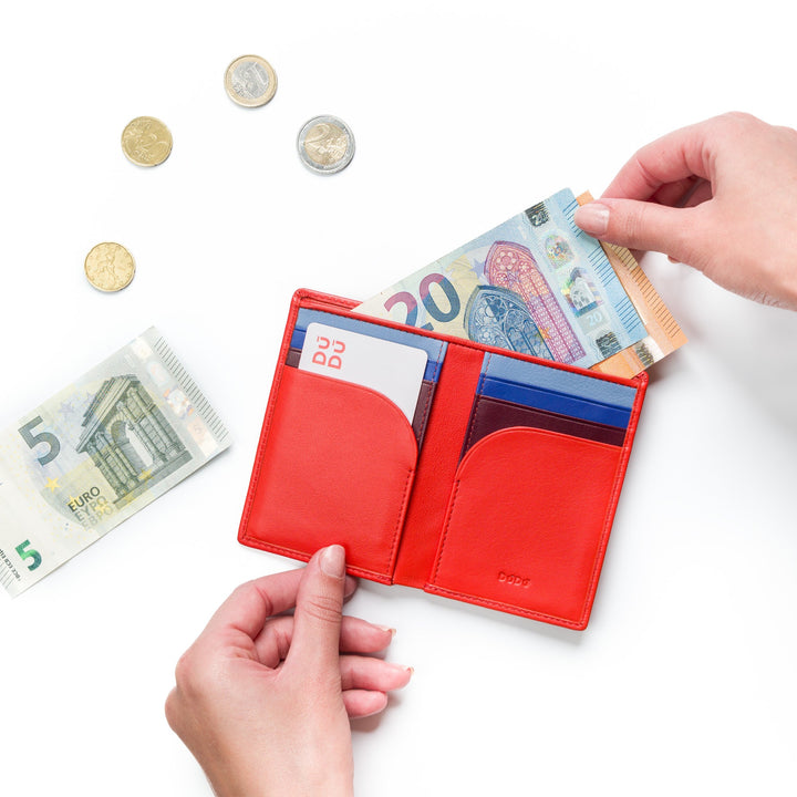 Hands holding a red wallet with banknotes and cards, surrounded by Euro coins and notes on white background