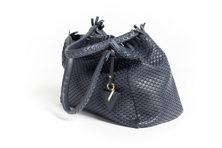 Elegant navy blue woven handbag with leather handles and a decorative pendant.