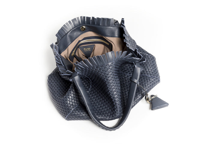 Elegant navy blue woven handbag with leather handles and a decorative pendant.