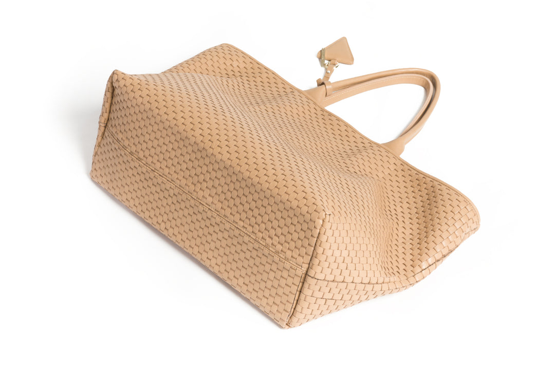 Handcrafted beige woven leather tote bag with dual handles and a triangular charm.