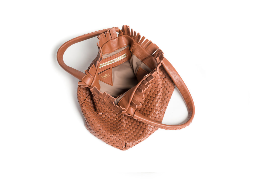 Tan woven leather handbag with fringe and tassel accents on a white background.