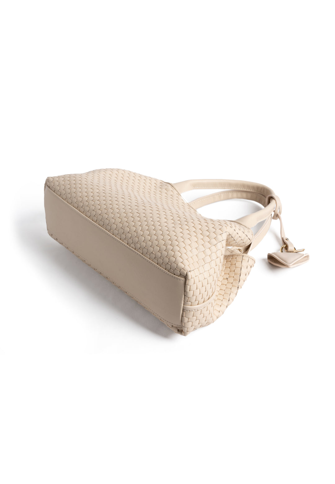 Elegant cream woven leather handbag with gold charm and sturdy handles, isolated on white background.