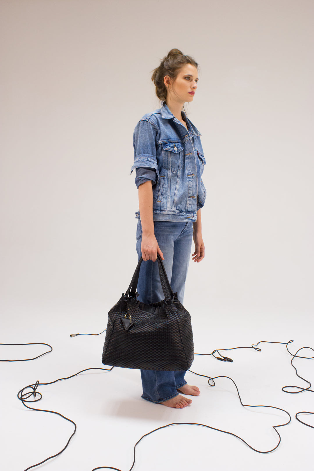 Black woven leather handbag with triangle pendant on white background.