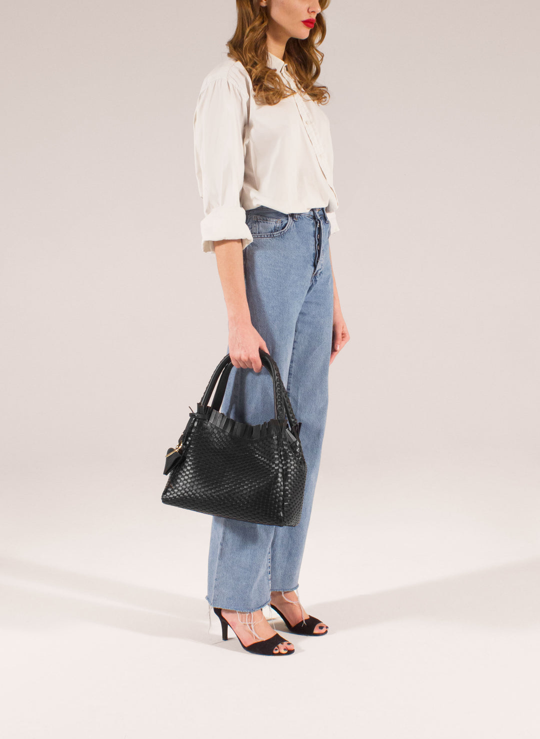 Black woven leather handbag with brown leather accent and triangular buckle on white background.