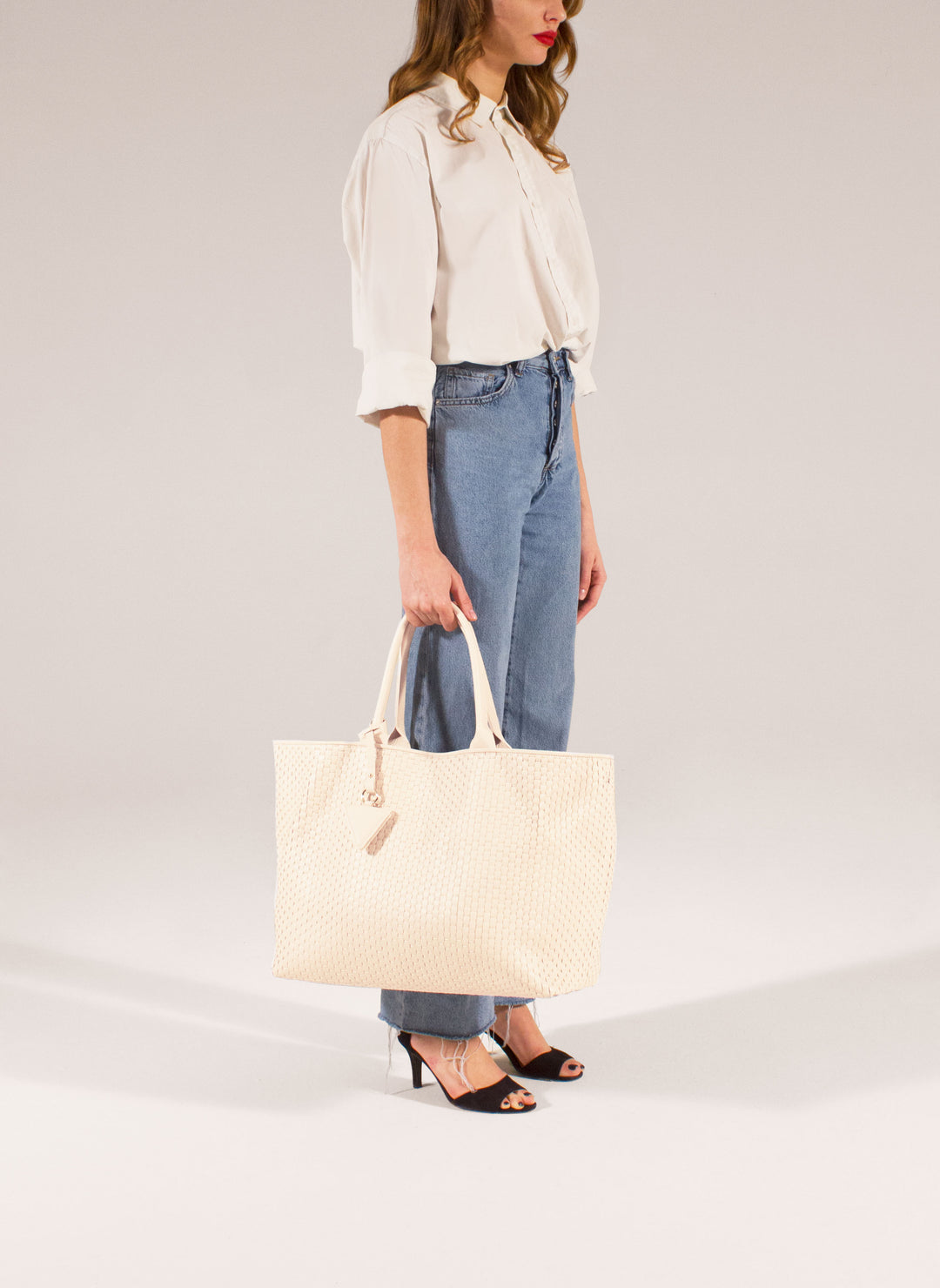 Cream-colored woven leather tote bag with handles and a triangular tag.