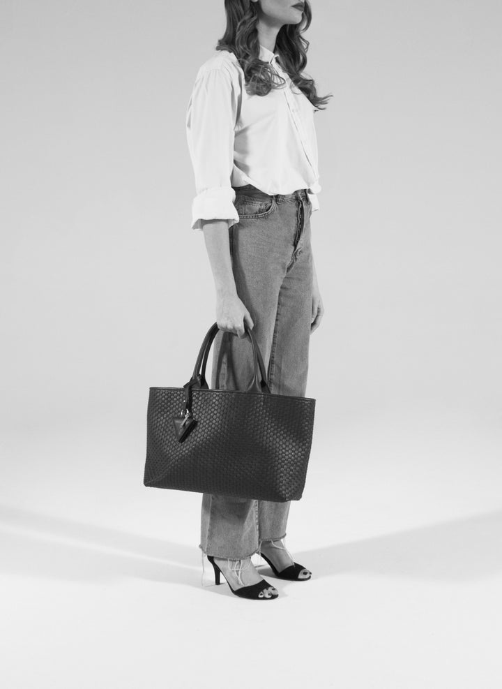 Beige woven tote bag with leather handles and a diamond-shaped keychain accessory.