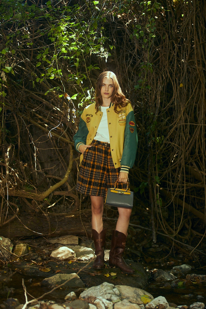 Young woman in a letterman jacket and plaid skirt standing in a forest