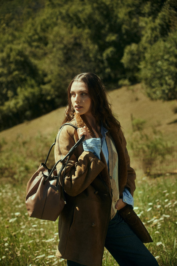 Woman in stylish autumn attire with handbag standing in a grassy field