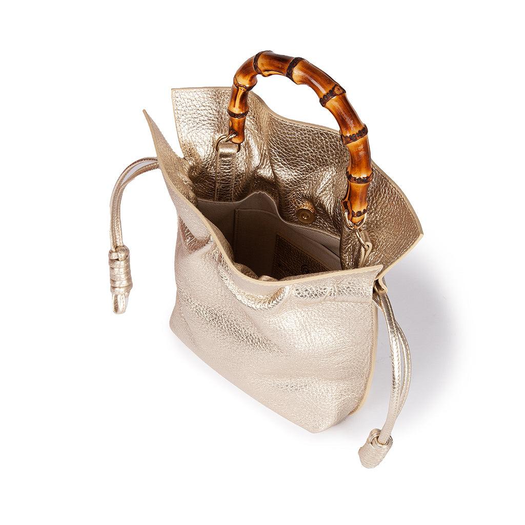 Gold leather handbag with bamboo handles, showing open top and interior pockets