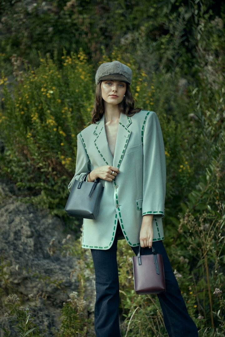 Woman wearing a stylish green blazer and hat outdoors, carrying fashionable handbags