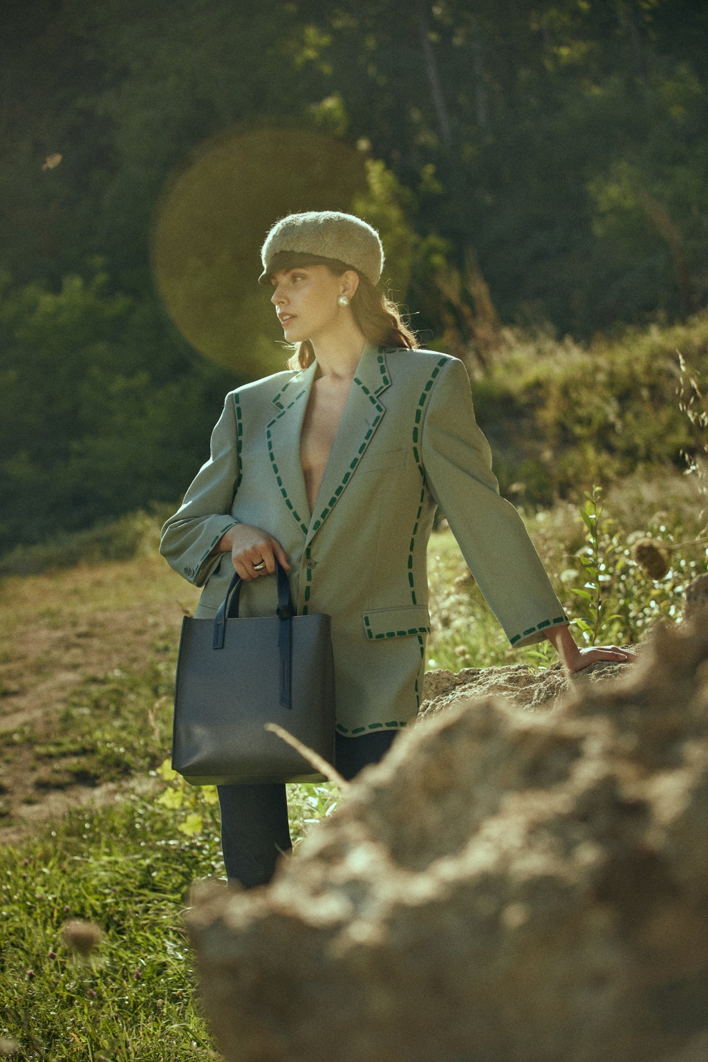 Woman outdoors wearing stylish green coat and hat, holding a navy handbag