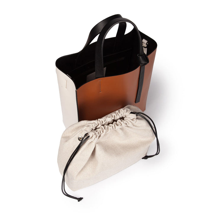 Two-tone leather tote bag with black handles and an accompanying beige drawstring pouch
