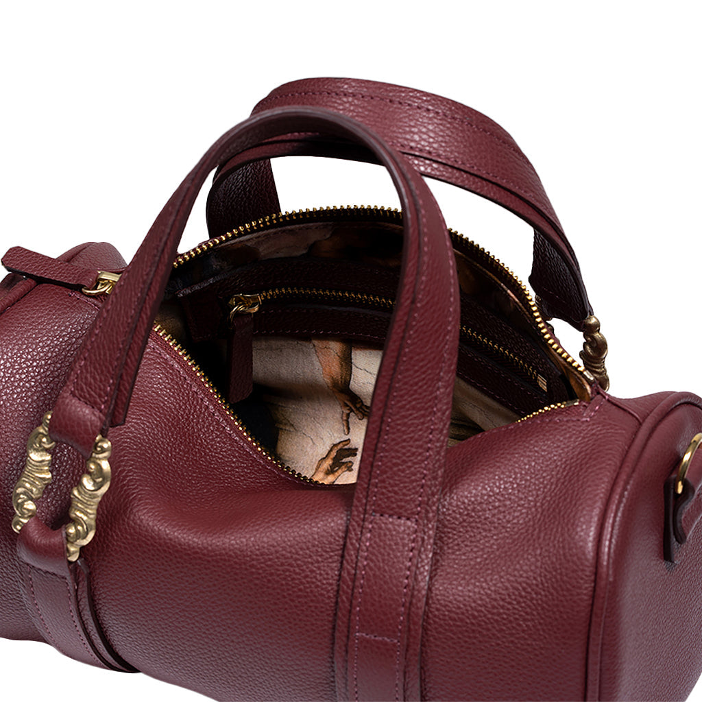 Maroon leather handbag with gold accents and partially opened zipper displaying interior compartments