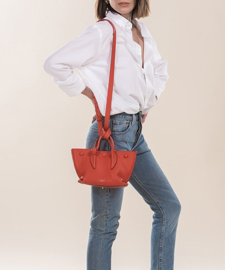 Woman wearing white blouse, blue jeans, and carrying a red leather handbag