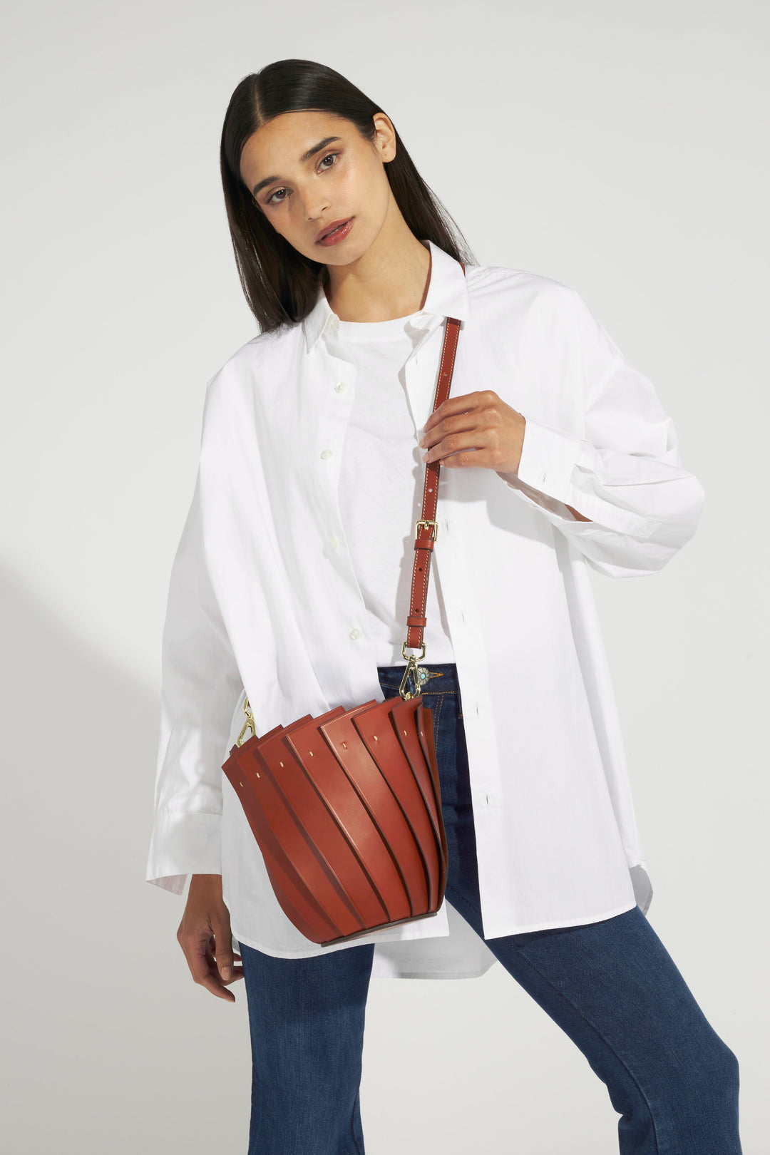 Woman wearing white shirt and jeans, holding a stylish brown leather handbag