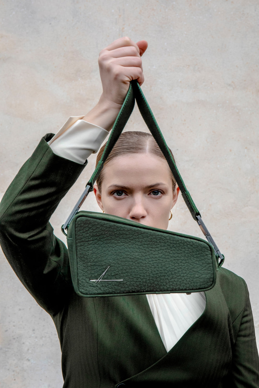 Woman holding a stylish green handbag in front of her face, dressed in a matching green outfit against a neutral background