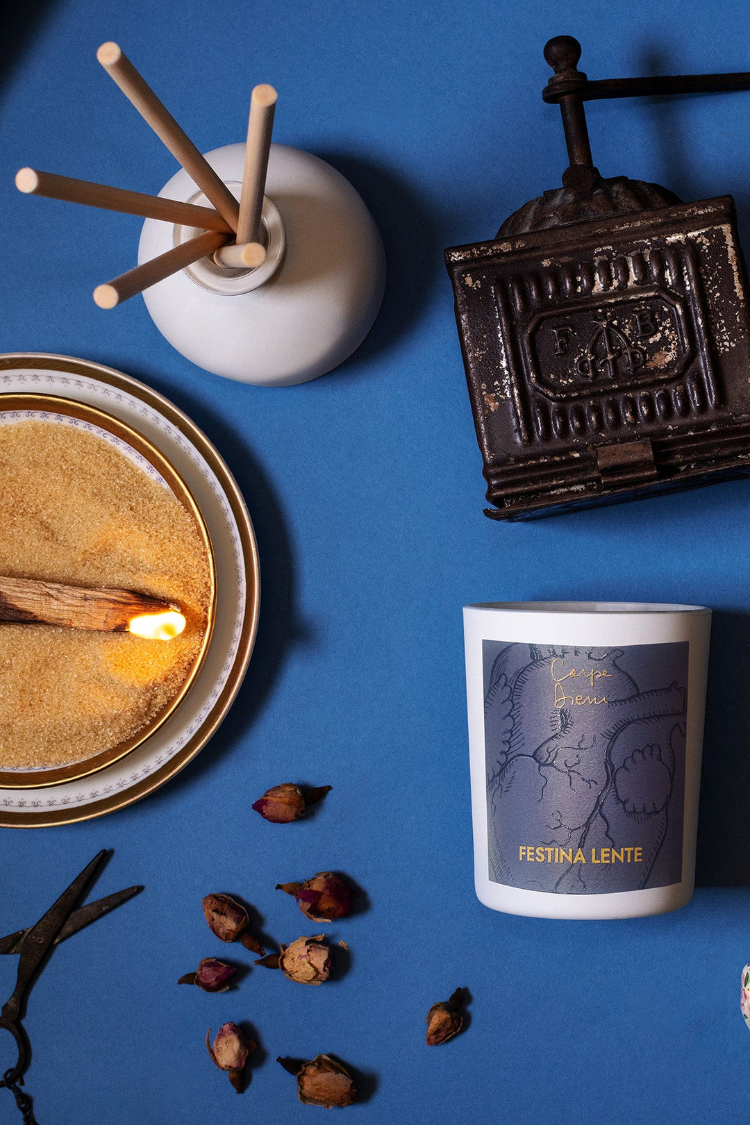 Overhead view of candle with lit match, vintage items, and dried flowers on blue background