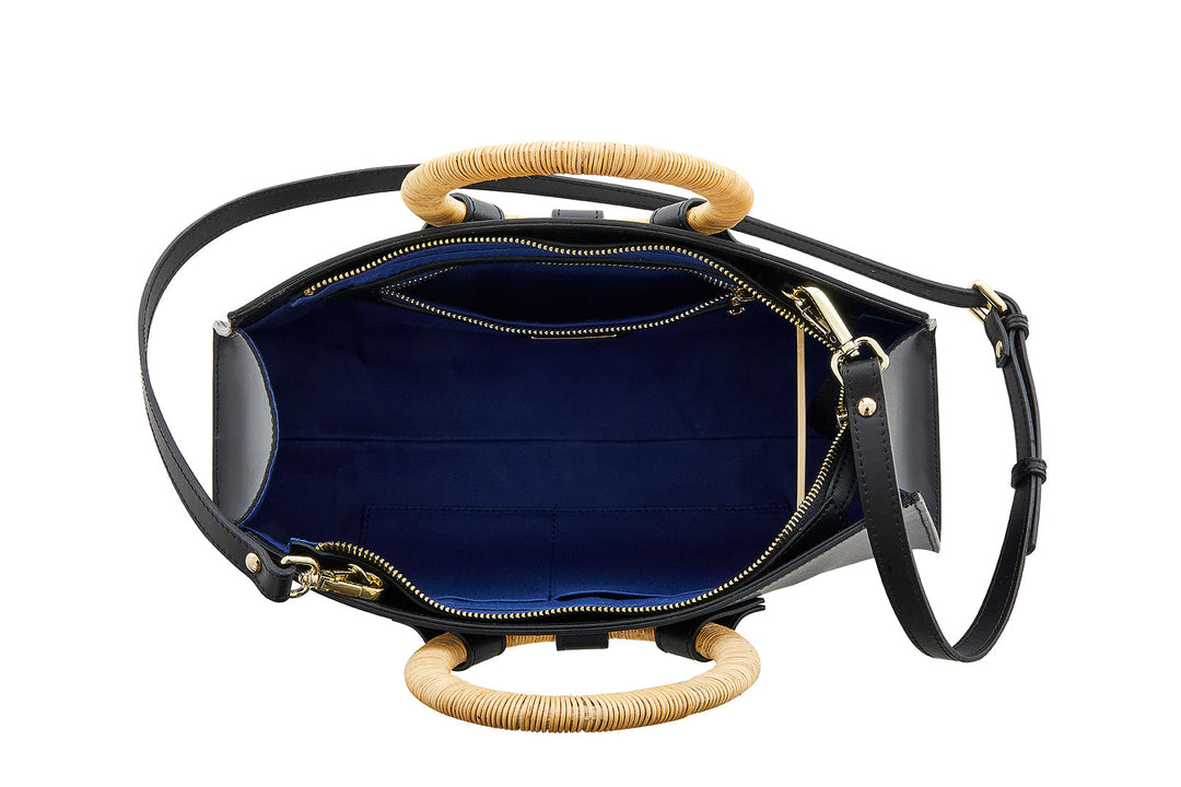 Top view of a black handbag with bamboo handles, open to show blue interior and zipper compartments