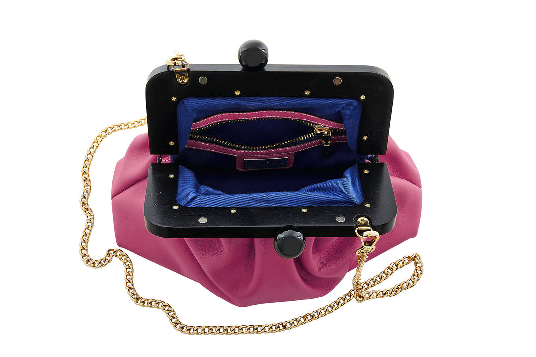 Pink leather clutch with a black frame, gold chain strap, and blue interior lining featuring a zippered pocket