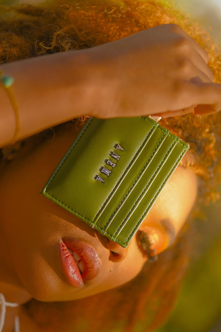 Close-up of a person holding a green leather cardholder over their eye