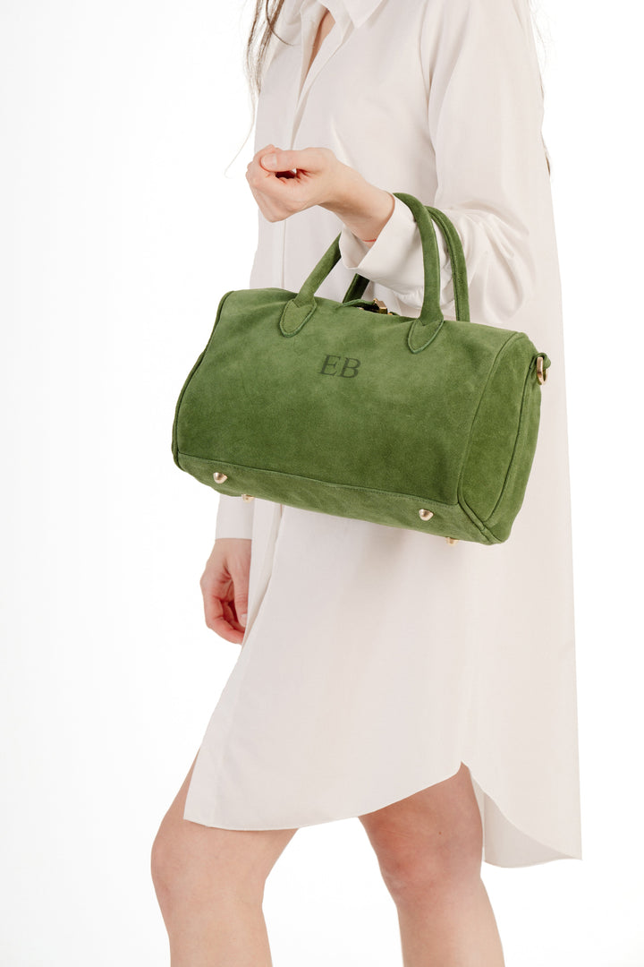 Woman holding a green suede handbag with initials EB