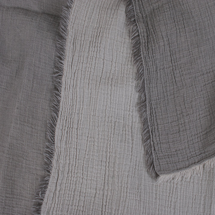 Close-up of folded gray and white textured fabric layers with fringed edges