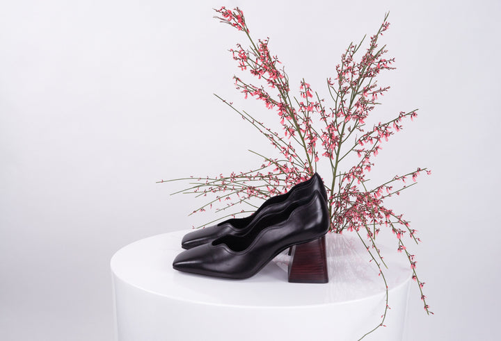 Black leather heels on white table with red floral branches in background