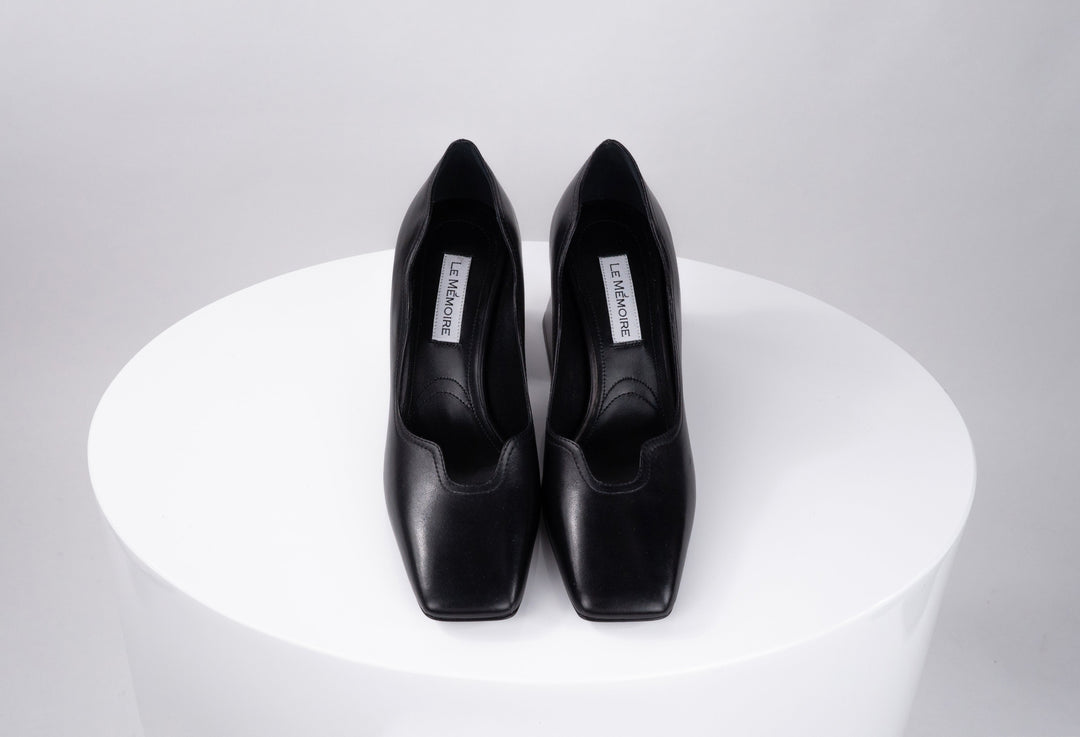 Pair of black leather high-heeled shoes on white round pedestal