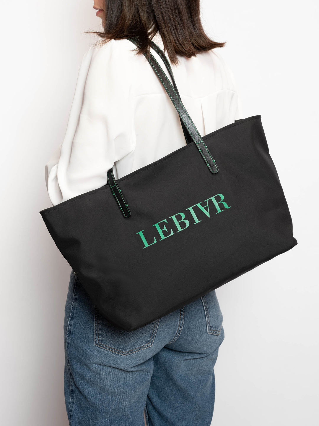 Woman carrying a black tote bag with LEBIVR text, wearing a white blouse and blue jeans