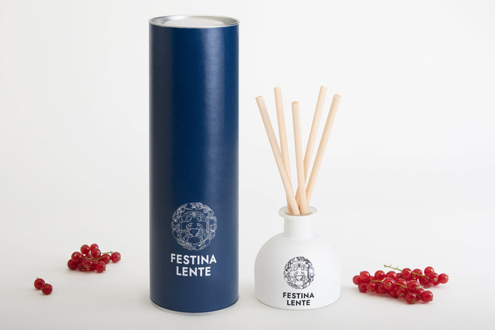 Aromatic diffuser set with blue cylindrical packaging and white diffuser jar with wooden sticks labeled Festina Lente