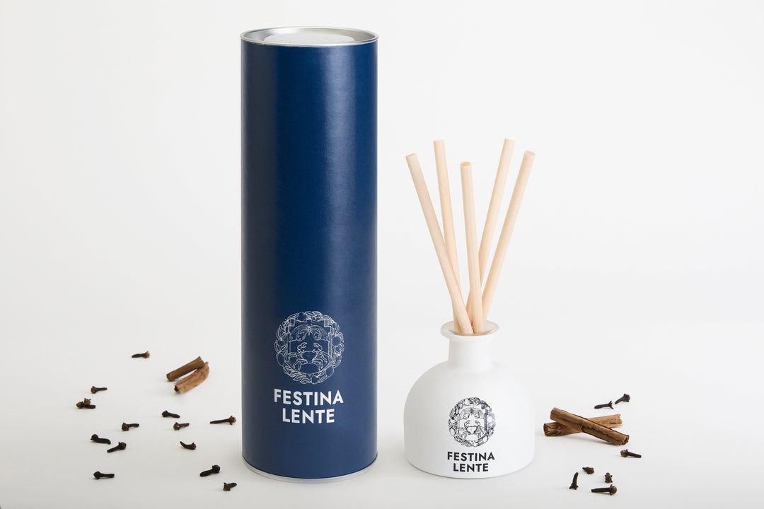 Aromatic reed diffuser with stylish navy blue and white packaging by Festina Lente, surrounded by natural spice fragments