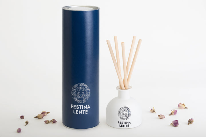 Festina Lente reed diffuser with navy blue cylindrical box and scattered dried flower petals