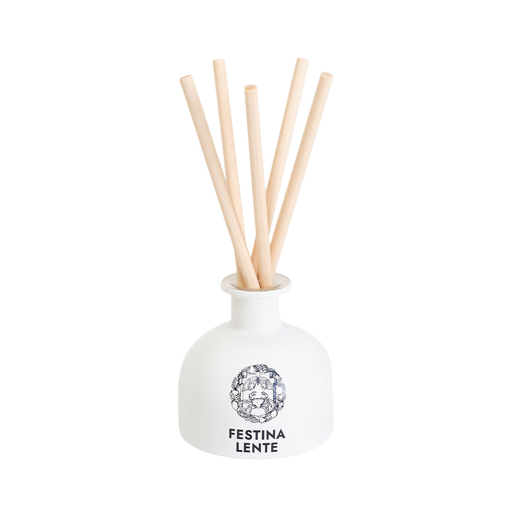 White ceramic reed diffuser bottle with natural wood sticks, labeled Festina Lente