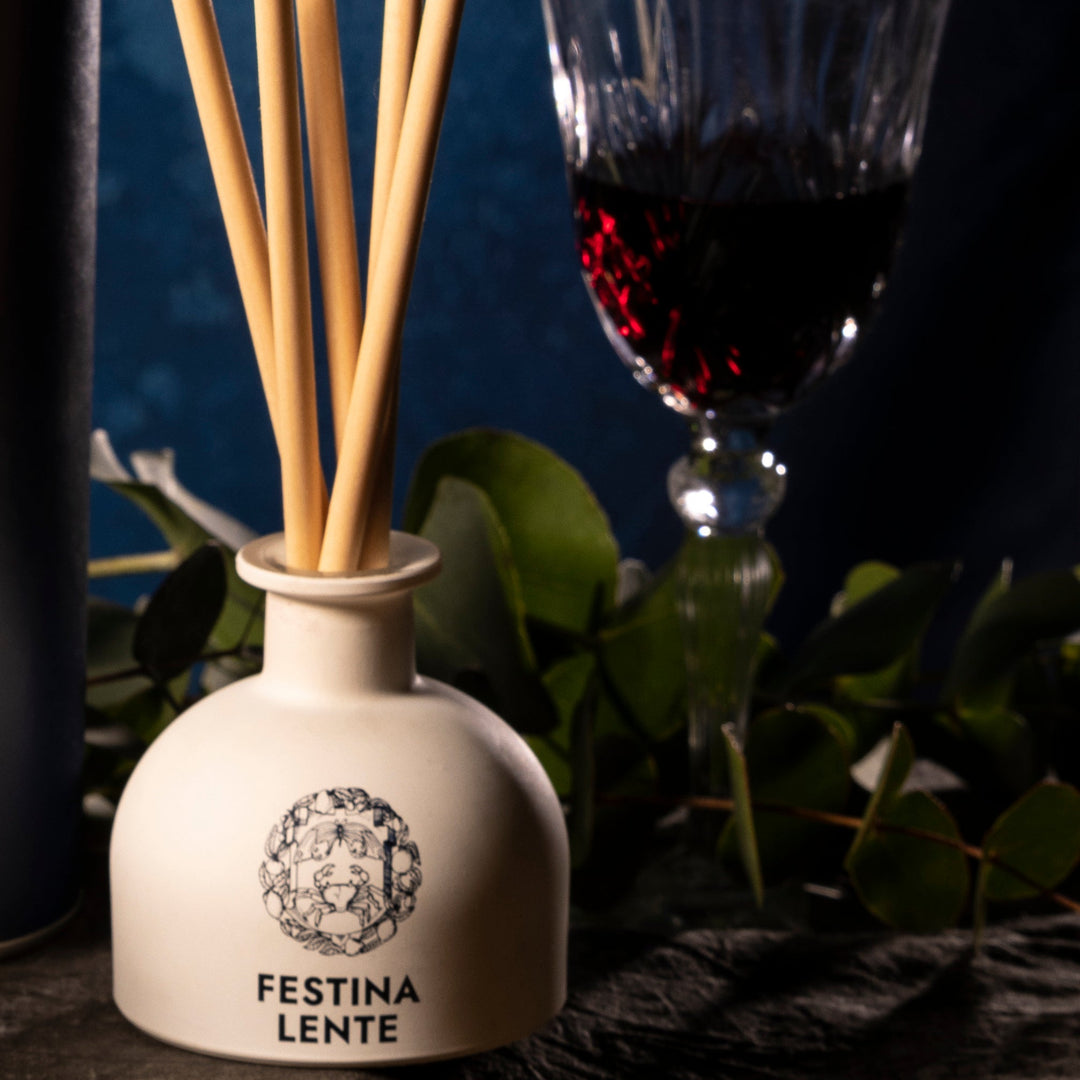 Aromatic diffuser bottle beside a glass of red wine on a table with green leaves