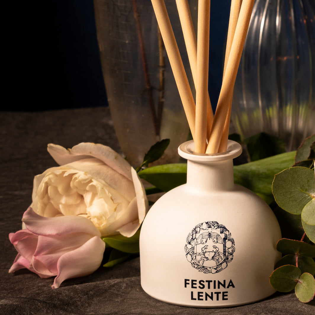 White flower diffuser bottle labeled Festina Lente with roses and greenery